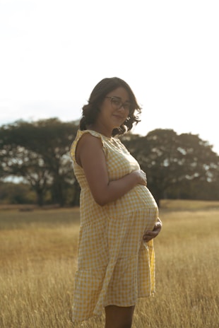 a pregnant woman standing in a field of tall grass
