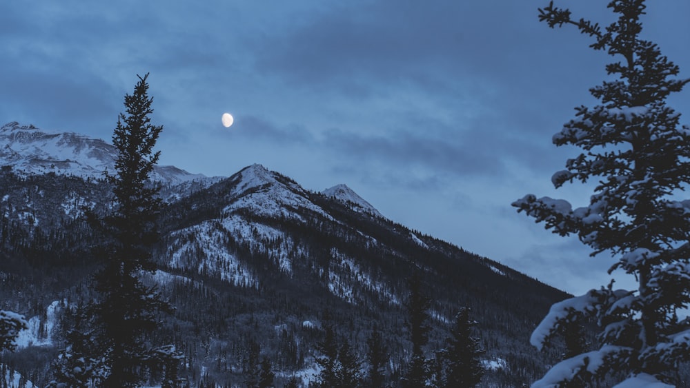 a full moon rises over a snowy mountain range
