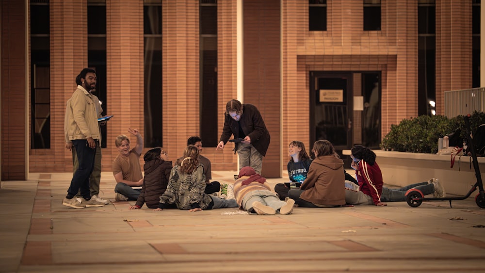 a group of people sitting on the ground in front of a building