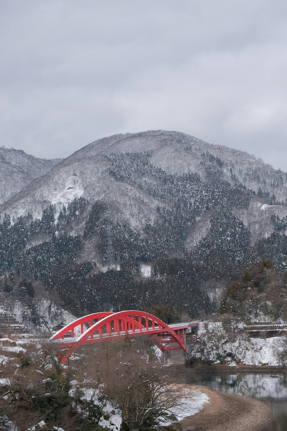 a red bridge over a river with a mountain in the background