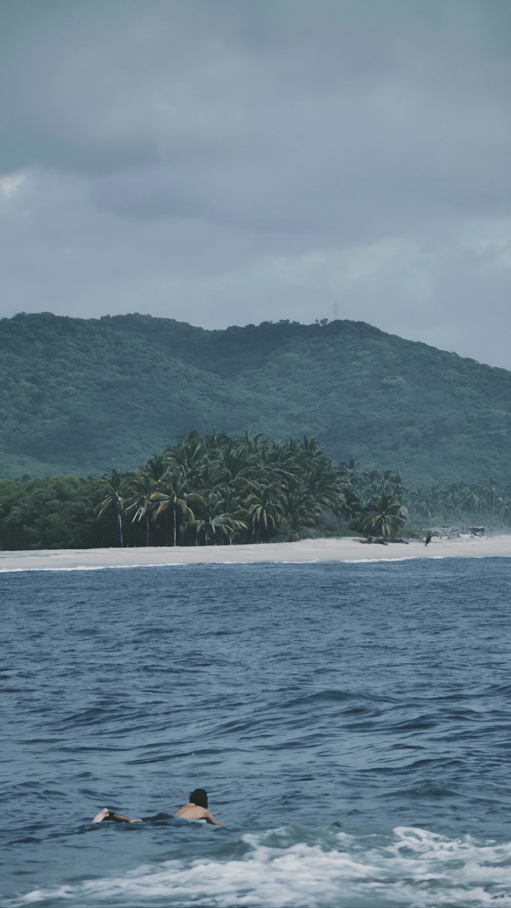 a person swimming in the ocean with a mountain in the background