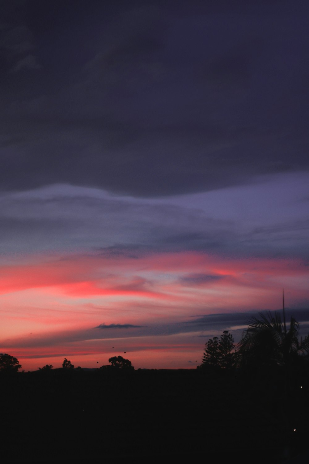 a red and purple sky with clouds and trees