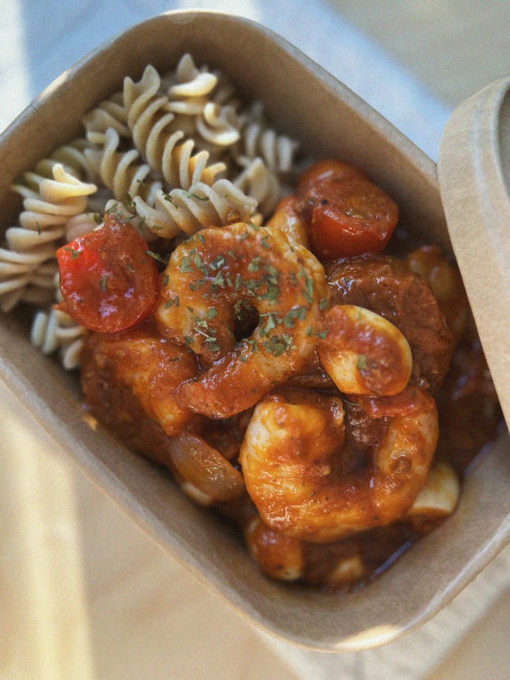 a container filled with pasta and shrimp with sauce