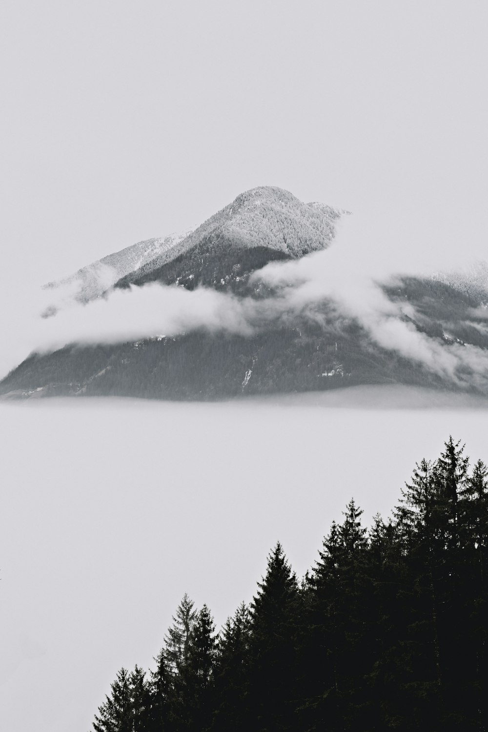 a black and white photo of a mountain covered in clouds