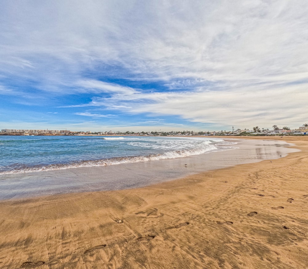 a sandy beach next to the ocean under a blue sky