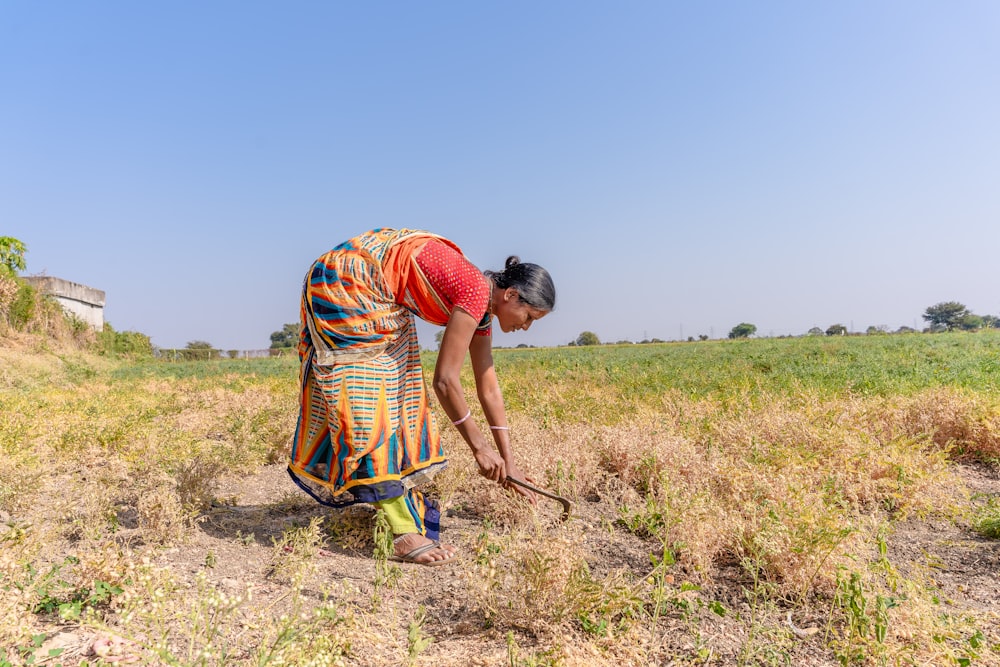 a woman kneeling down in a field with a stick