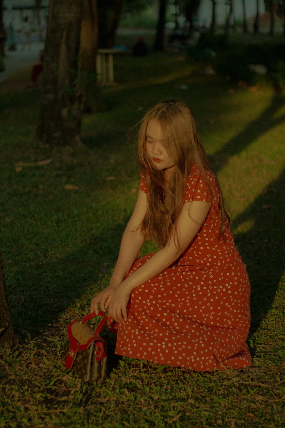 a young girl sitting on the ground next to a tree