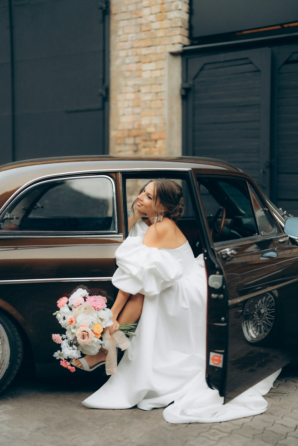 a woman in a white dress standing next to a brown car