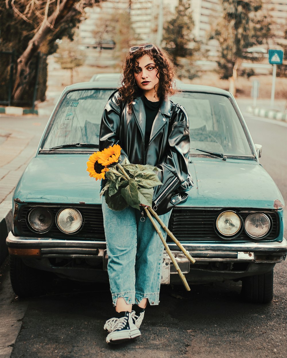 a woman sitting on the hood of a car holding a bouquet of flowers