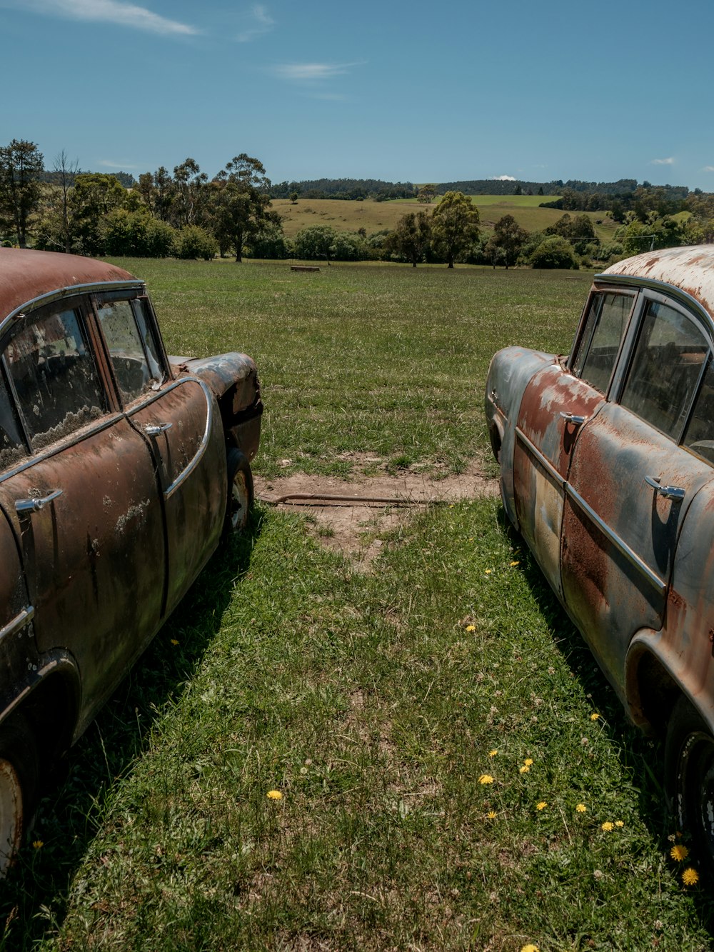 two old rusted cars sitting in a field