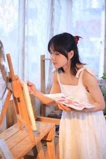 a woman in a white dress is painting a picture