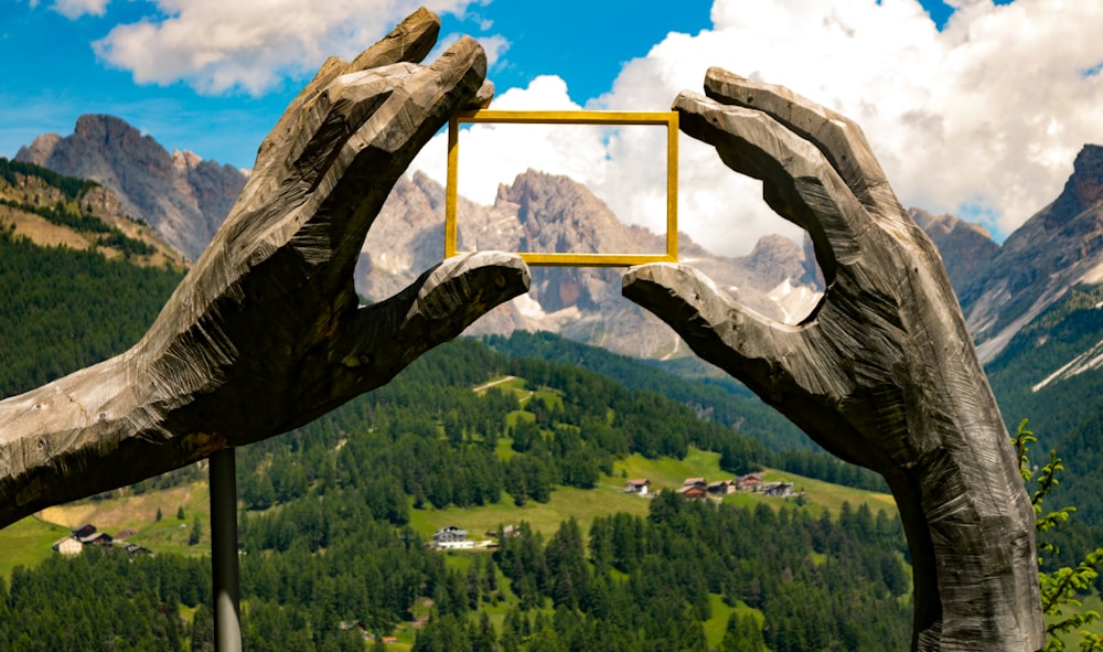 a pair of hands holding a small square in front of a mountain range