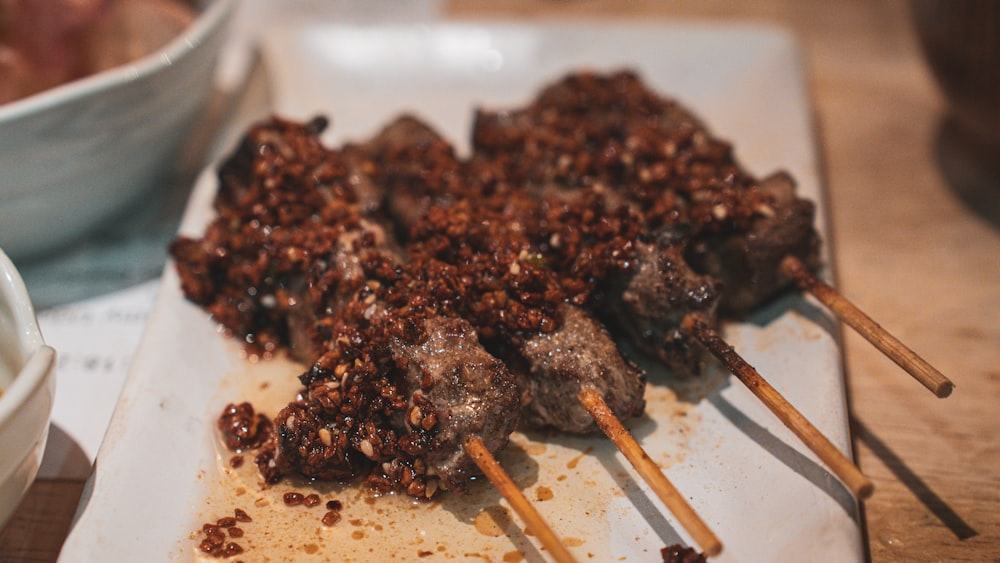 un plato blanco cubierto con brochetas de carne y salsa