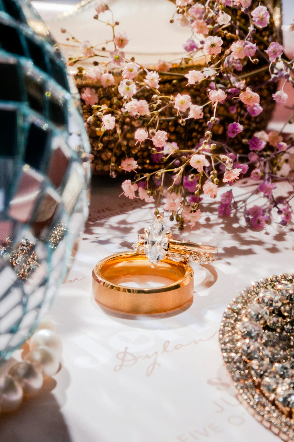 a table topped with two wedding rings and a vase filled with flowers