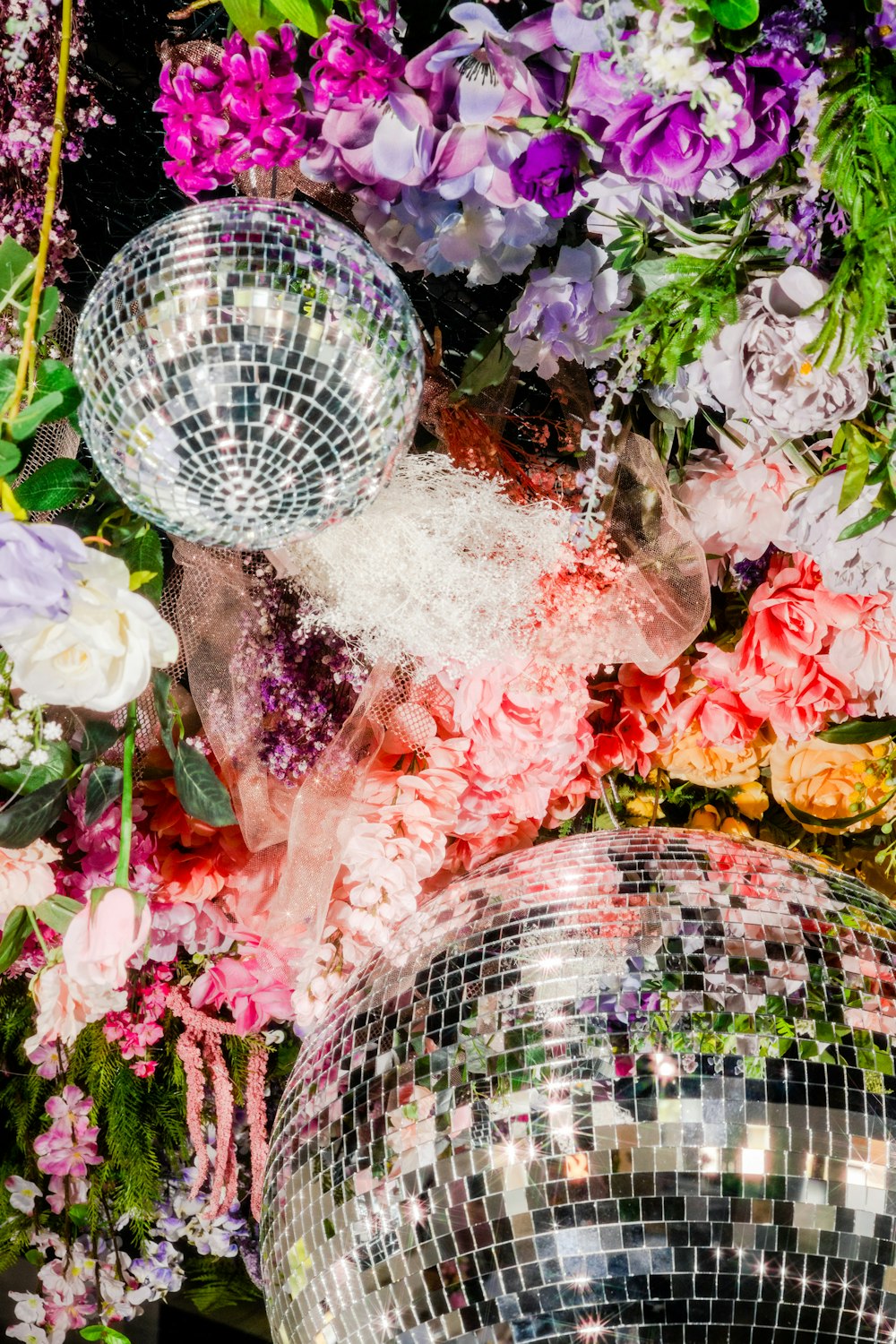 a bunch of disco balls sitting next to a bunch of flowers