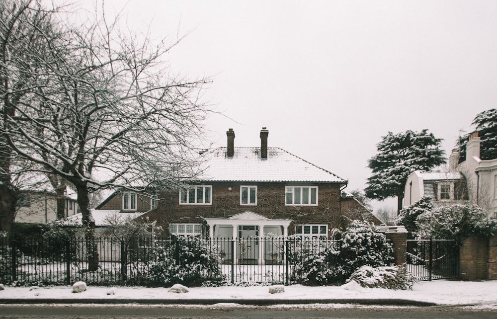 a red brick house with a white fence and snow on the ground