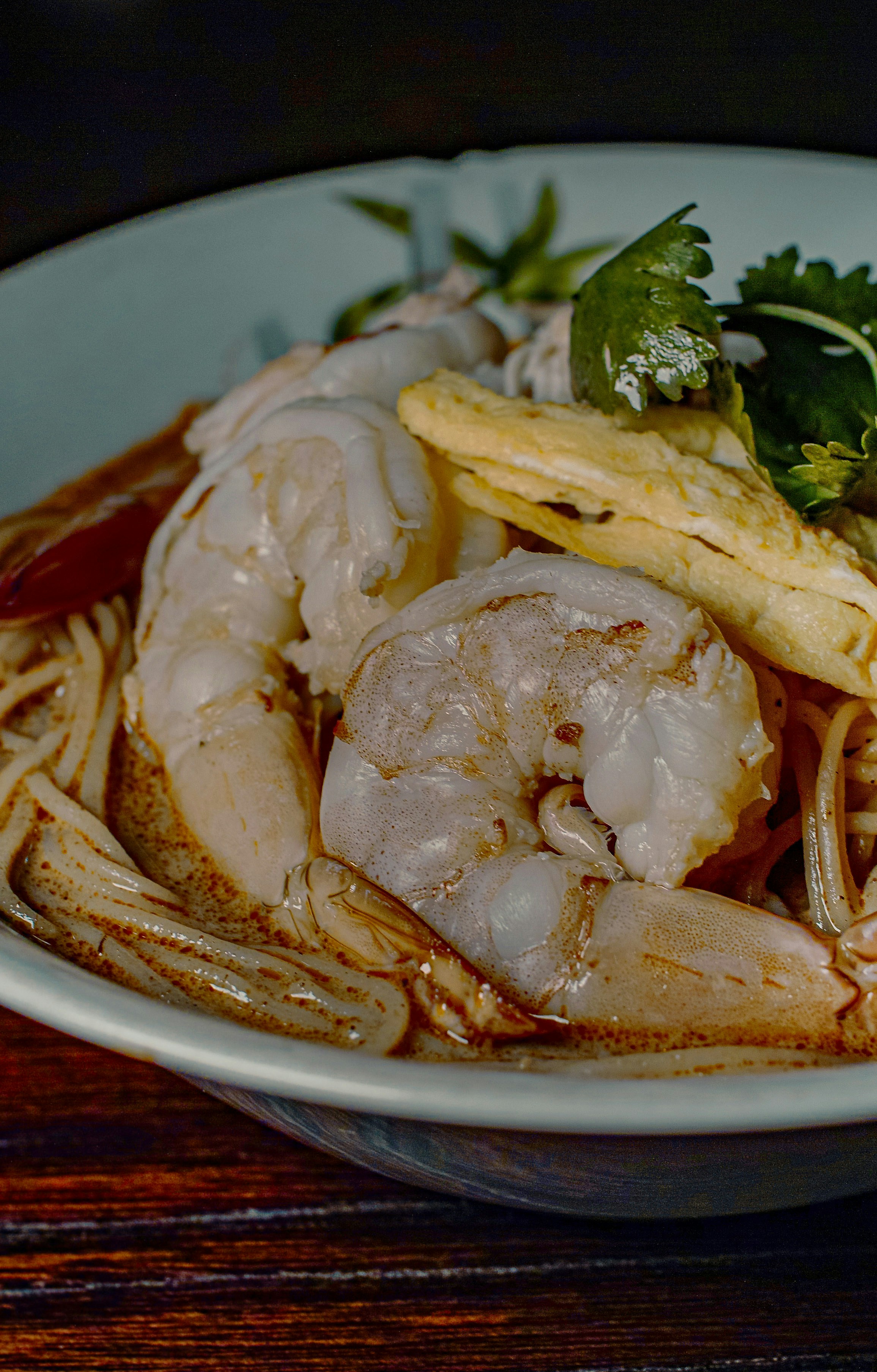 A bowl of curry noodle soup with large prawns, fried tofu and herbs