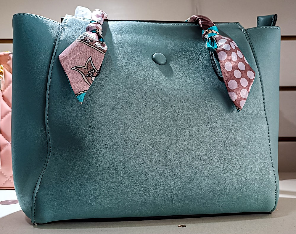 a blue purse with a pink polka dot scarf on it