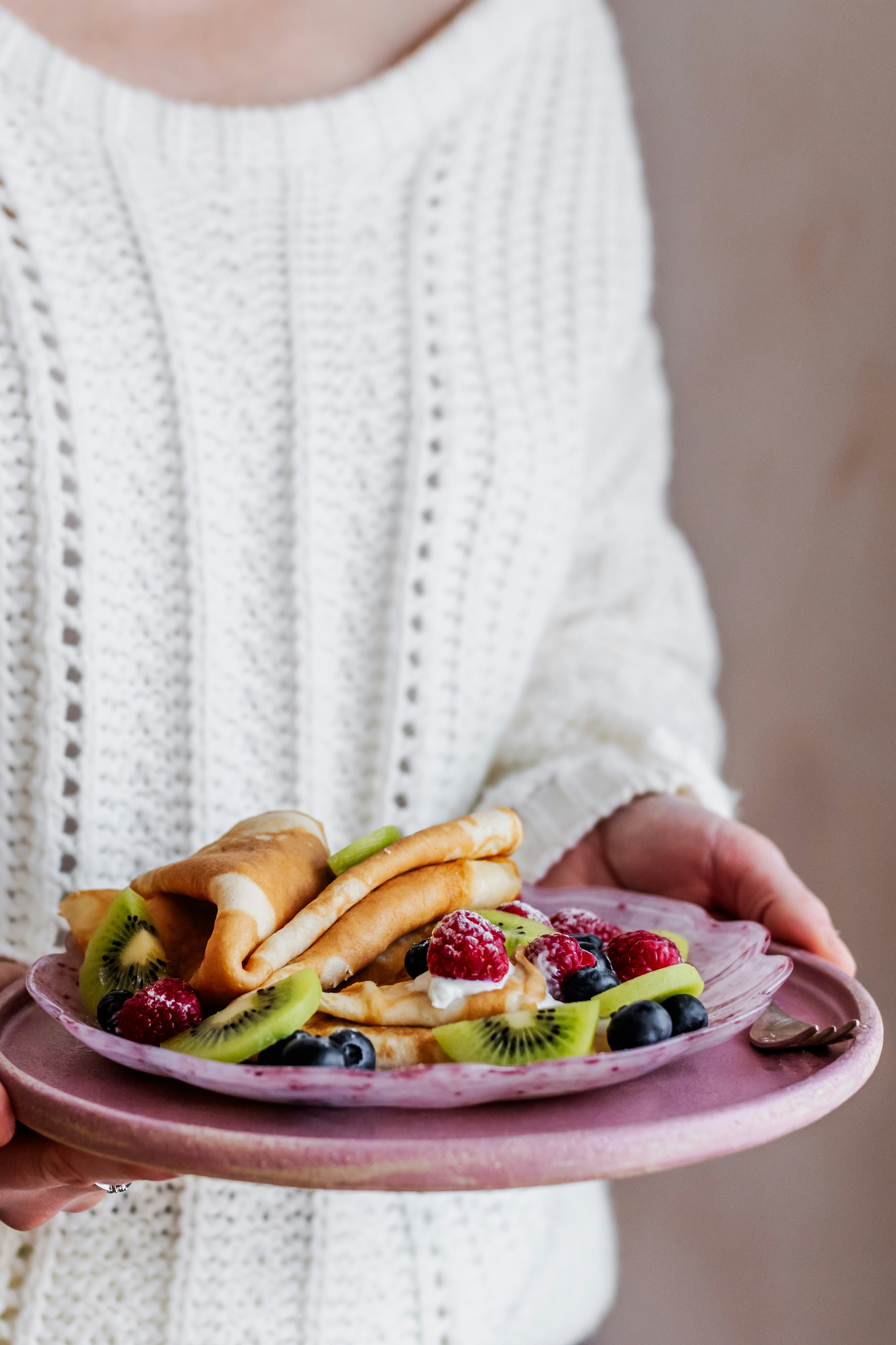 a woman holding a plate of fruit and pastry