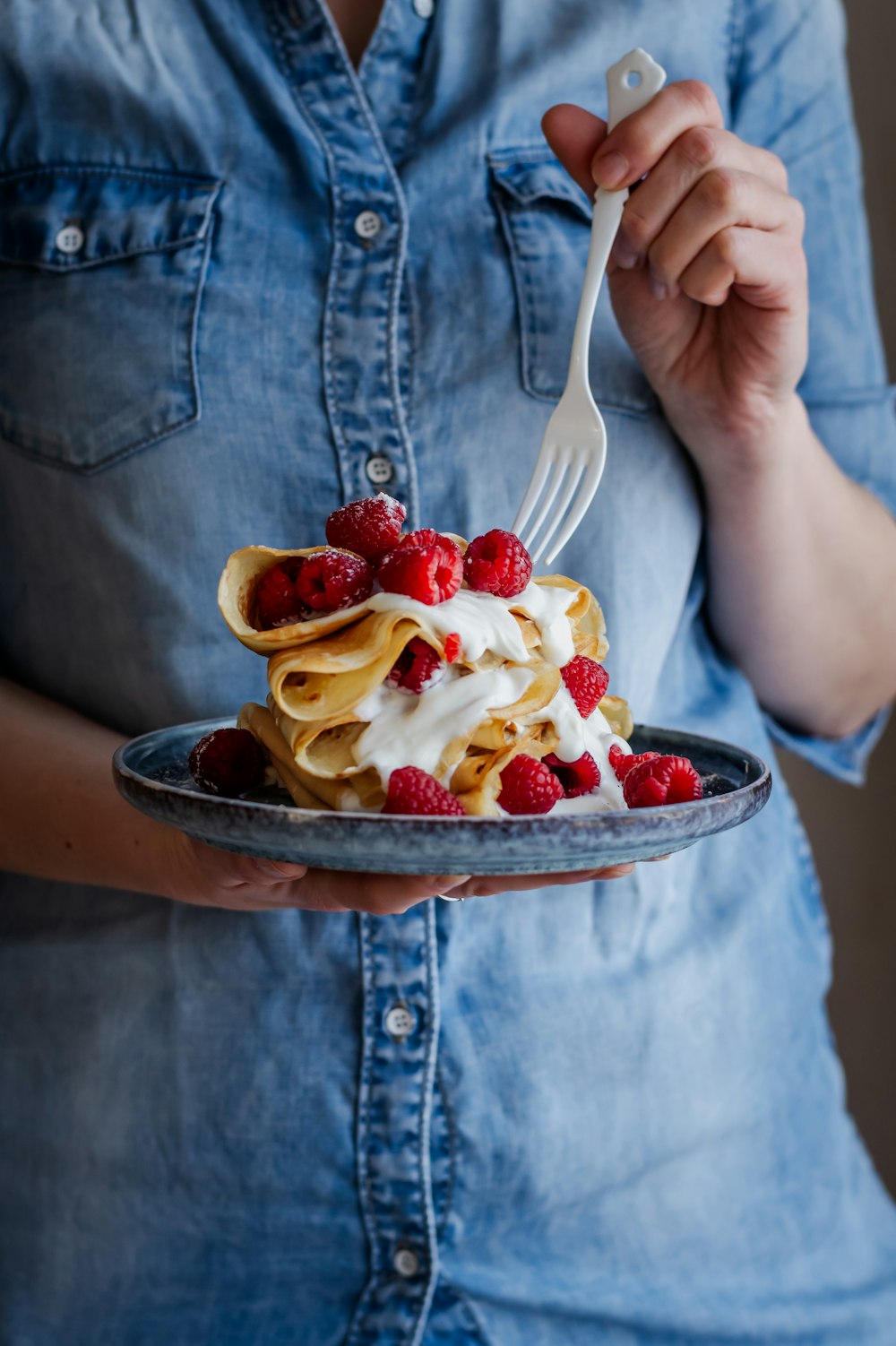 a woman holding a plate of food with a fork in it