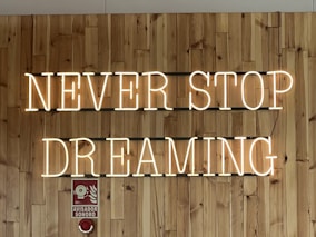 a wooden wall with a neon sign that says never stop dreaming