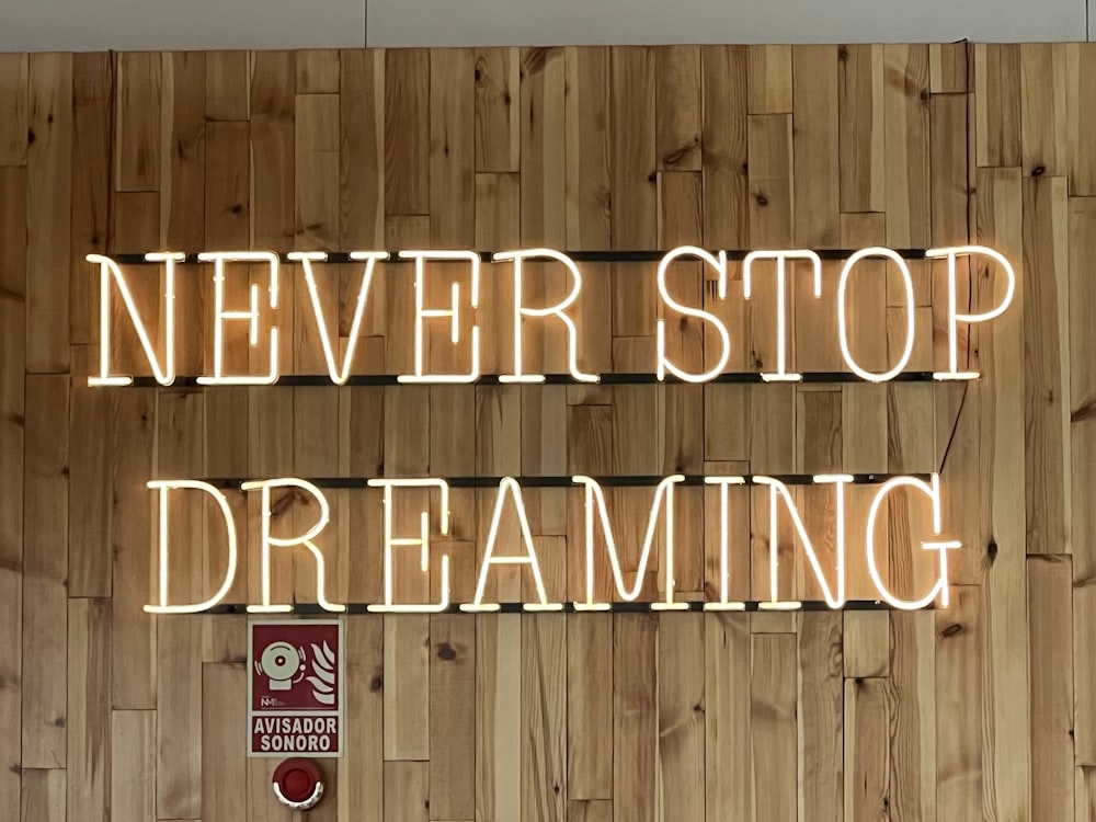 「Never Stop Dreaming」と書かれたネオンサインのある木製の壁