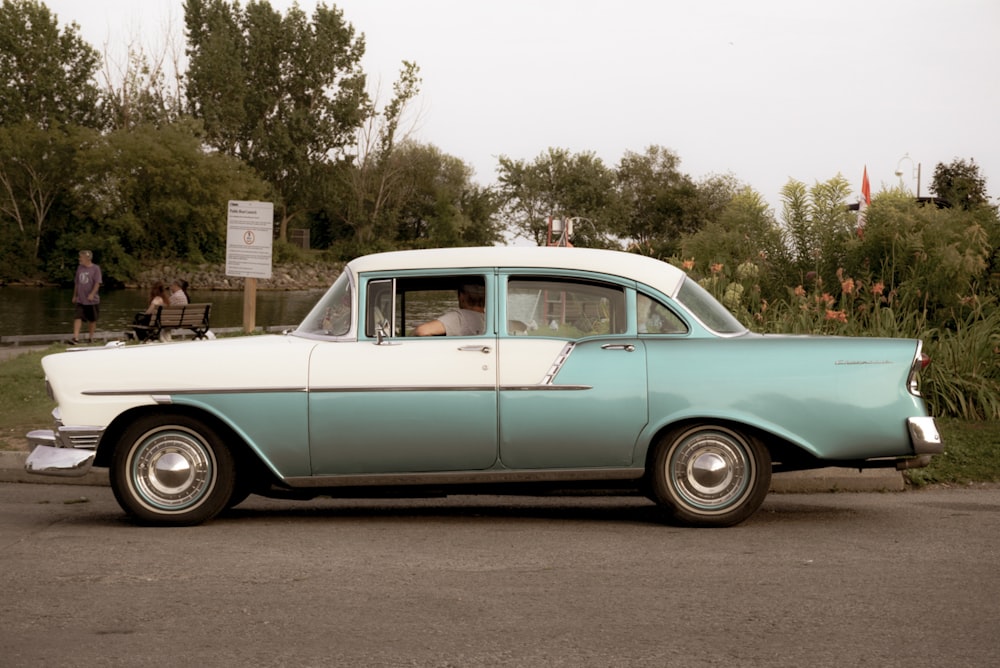 an old blue and white car parked on the side of the road