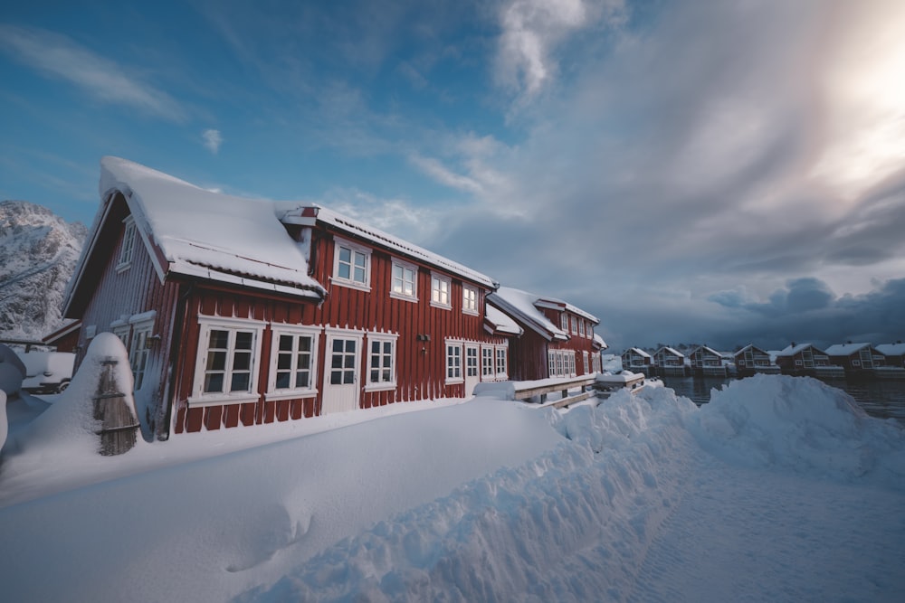 a red house covered in snow next to a body of water