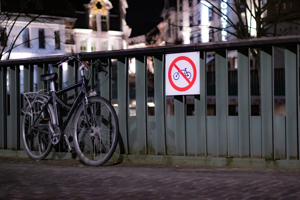 a bicycle parked next to a fence with a sign on it