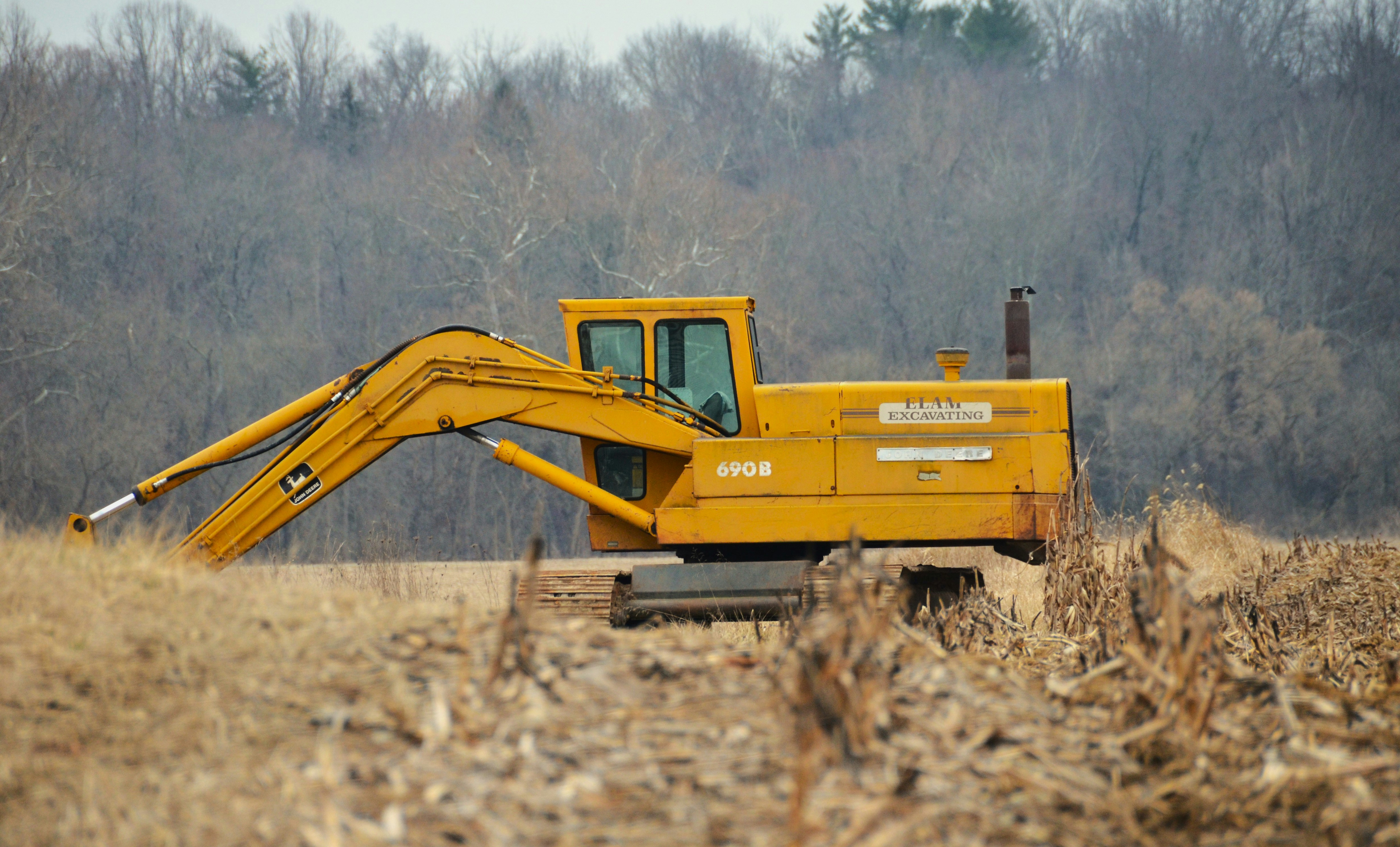 Excavator positioned in an open field with a tree line along the horizon