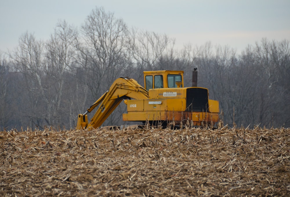 a yellow bulldozer in a field with trees in the background