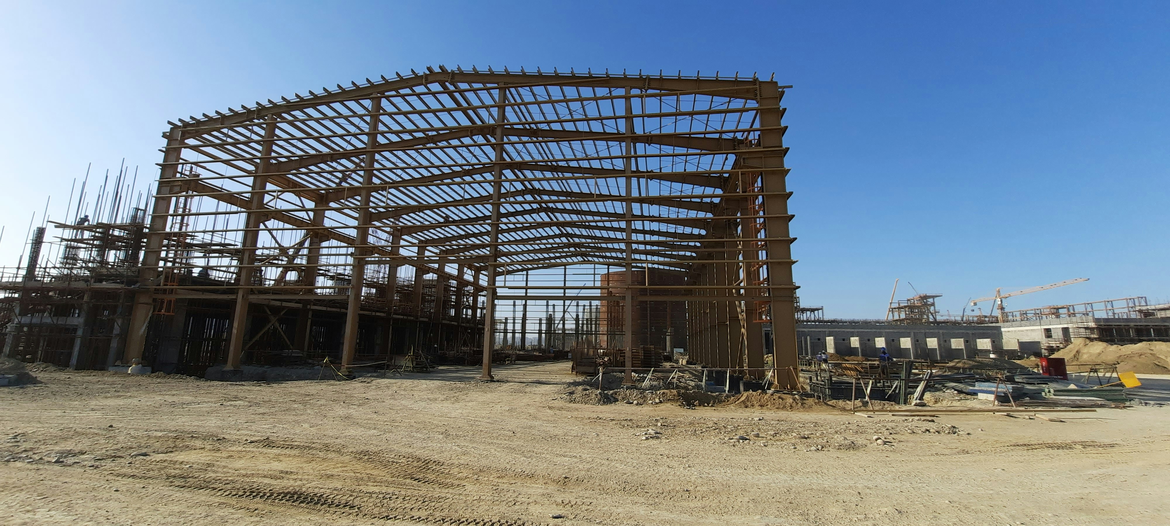 Steel building frame under construction with blue sky, structural steel beams, industrial construction site bright daylight