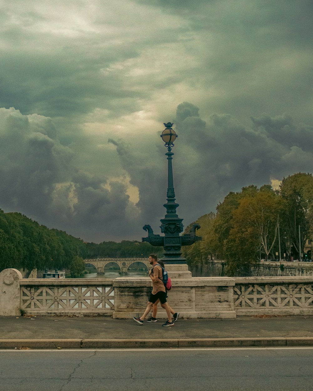 a man walking across a bridge under a cloudy sky