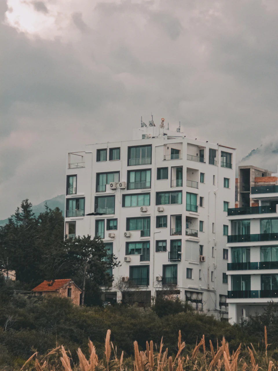 White modern building with multiple windows and balconies on a hillside surrounded by vegetation