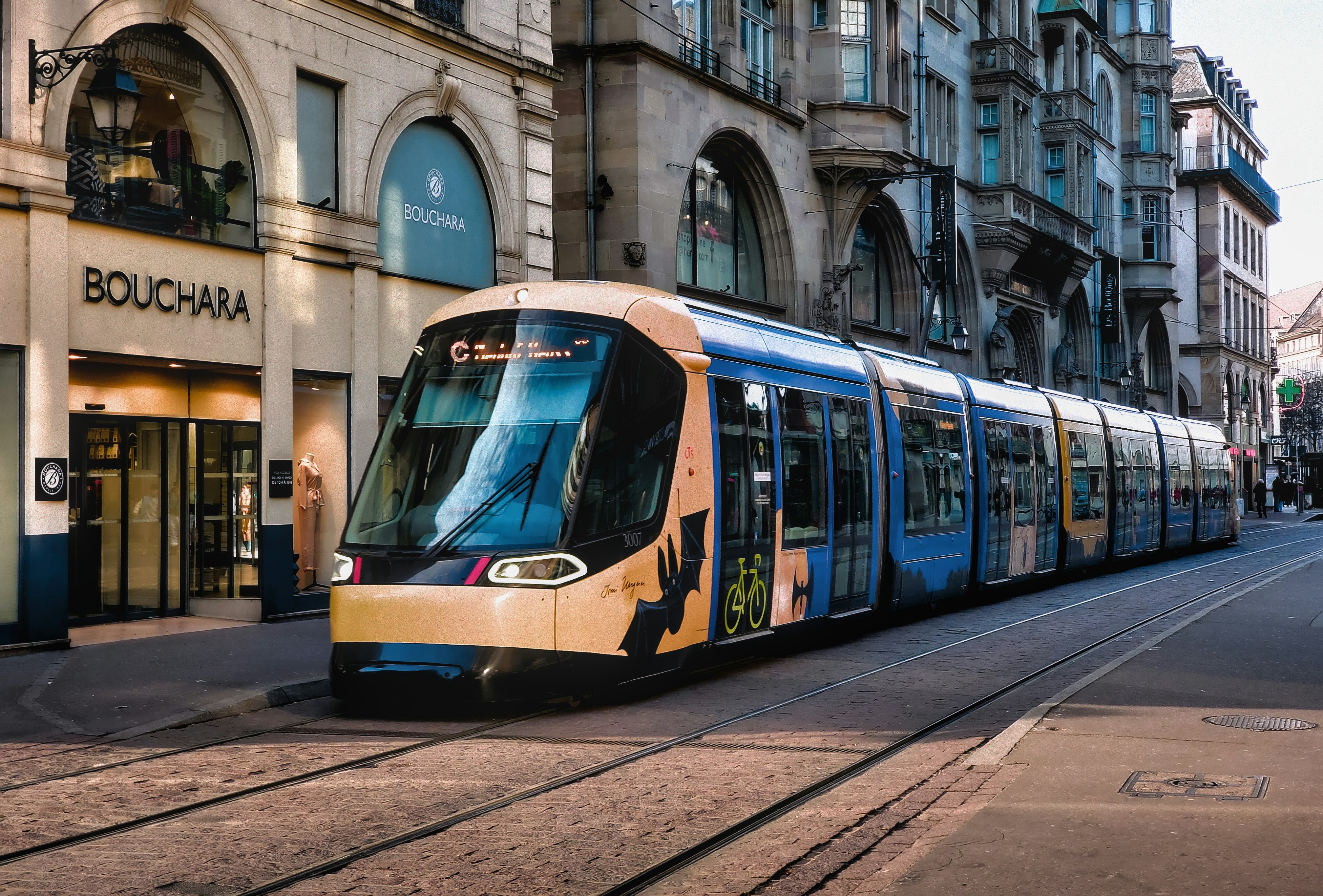a yellow and blue train traveling past a tall building, I wish the tram was not too crowded ...