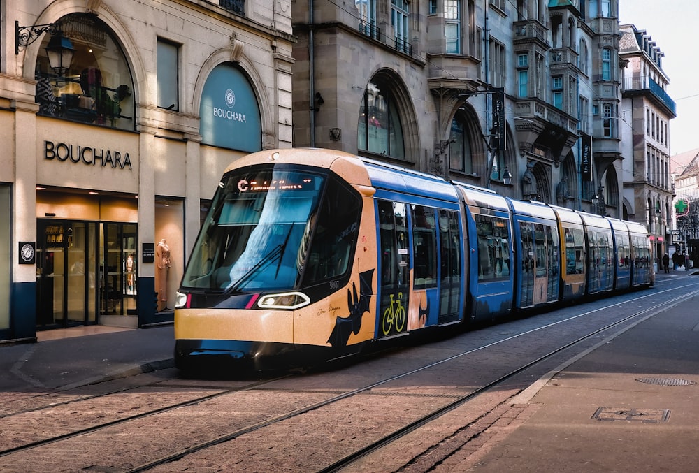 a yellow and blue train traveling past a tall building