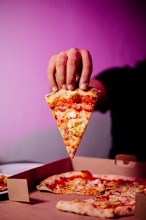 a person grabbing a slice of pizza from a box