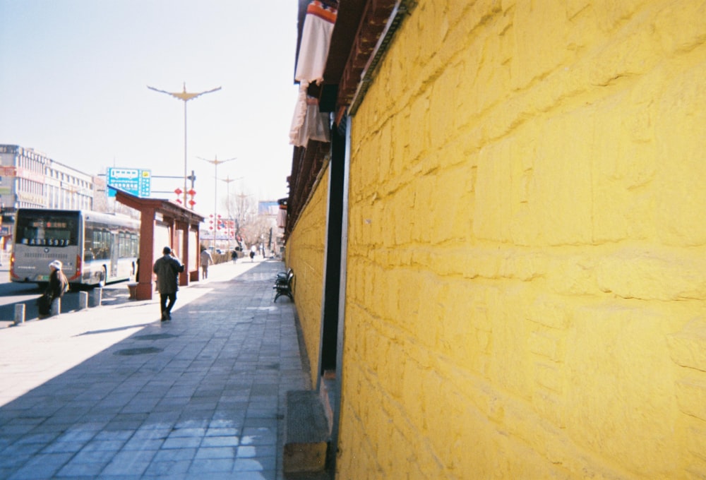 a man walking down a sidewalk next to a yellow wall