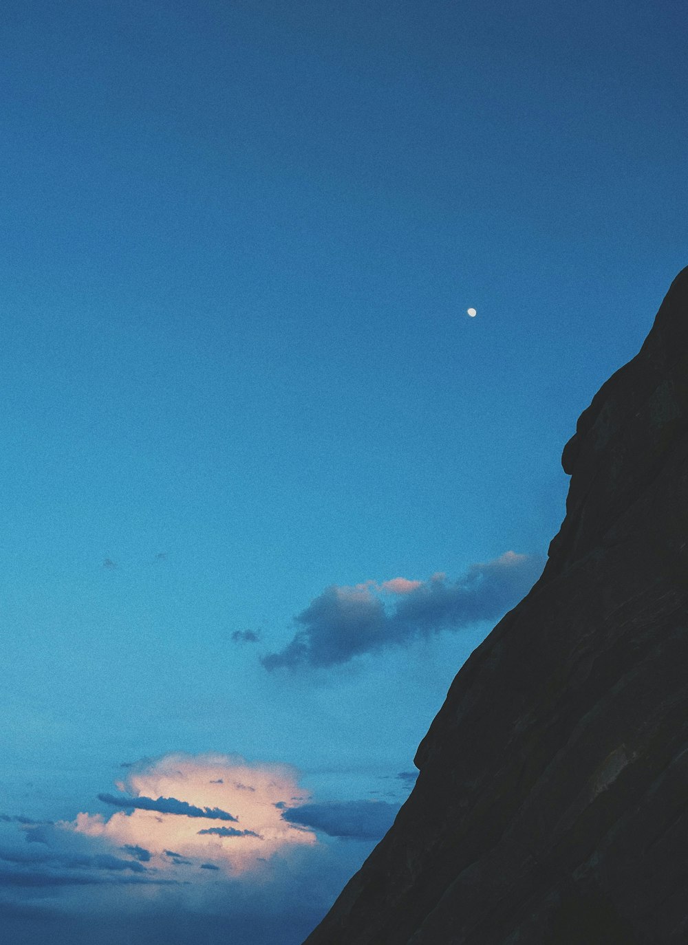 the moon is setting behind a mountain peak