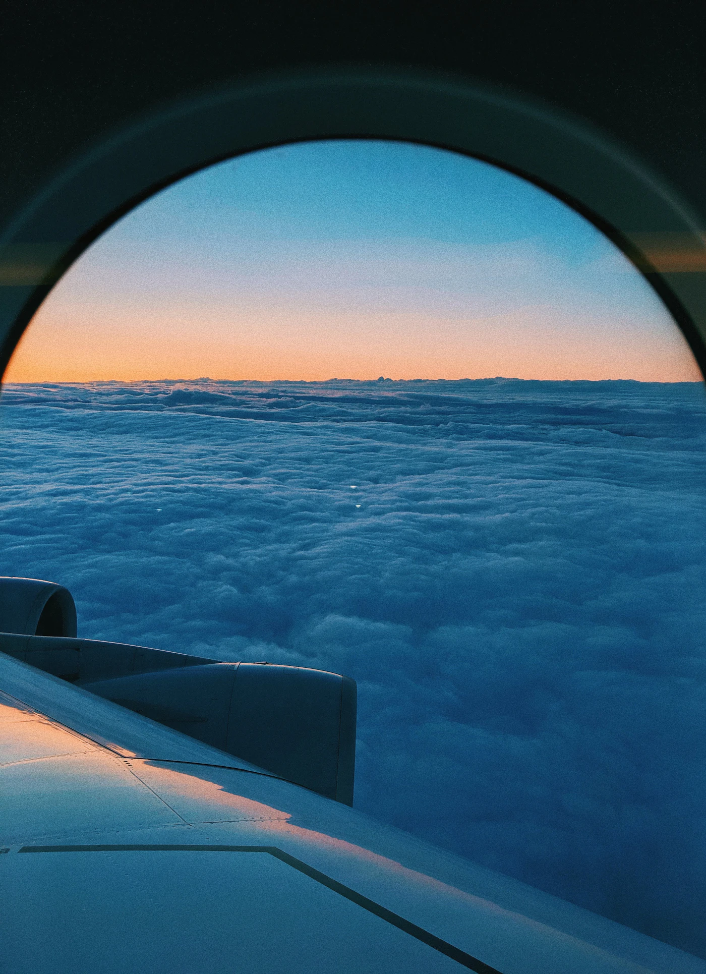 View through an airplane window of the wing above a soft layer of clouds at sunset during a calm flight