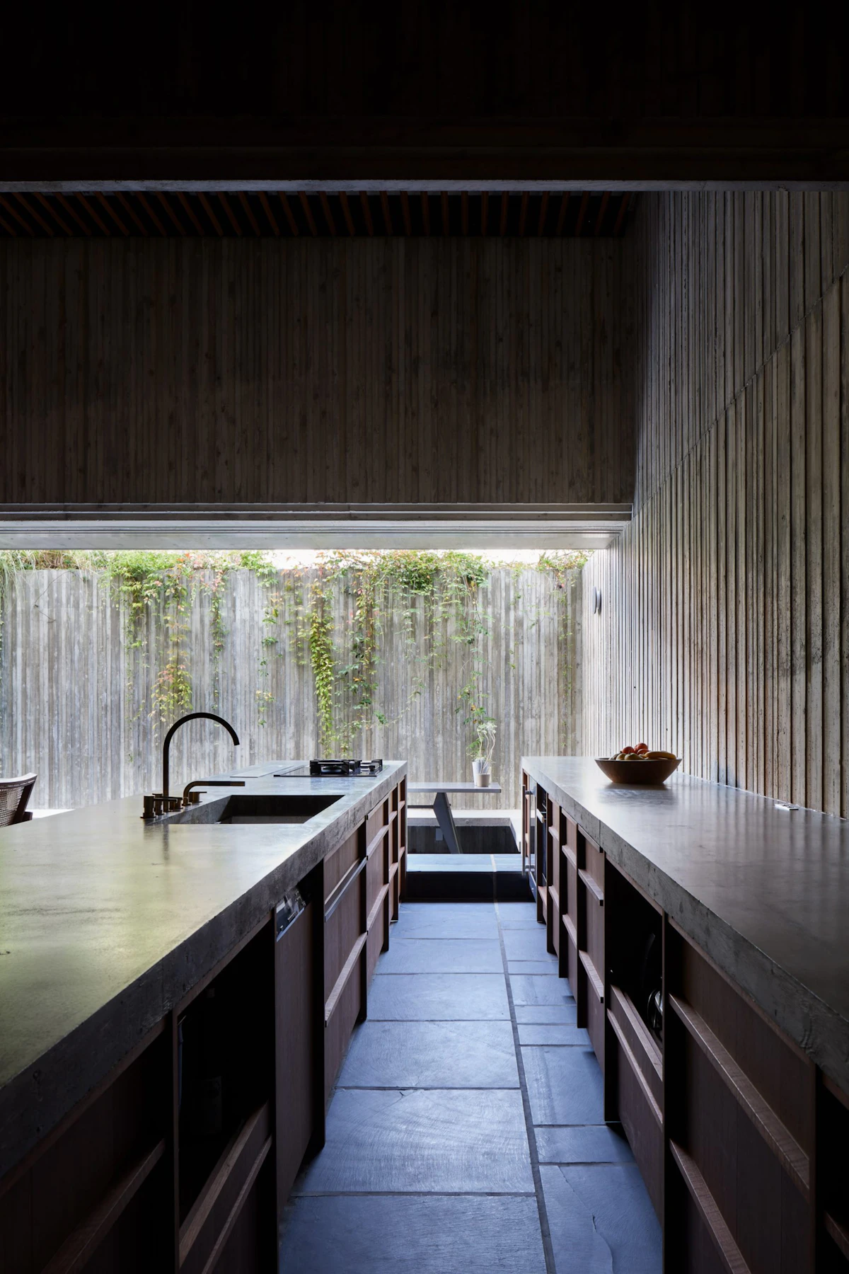 A striking modern minimalist kitchen featuring seamless gray concrete countertops, open storage shelving, and matte black steel pipes.