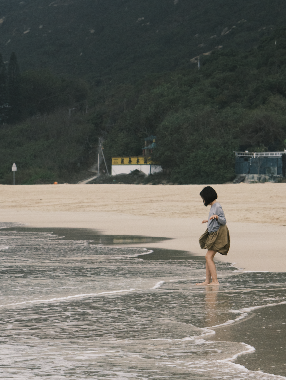 a woman standing on top of a sandy beach next to the ocean