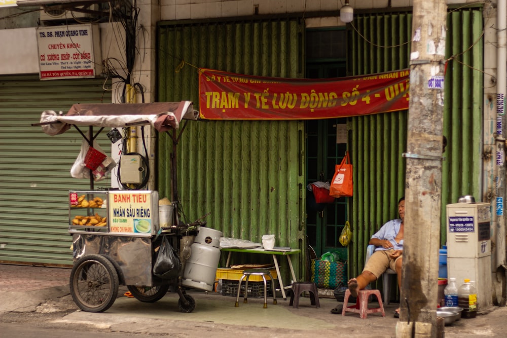 a man sitting on a chair in front of a food cart