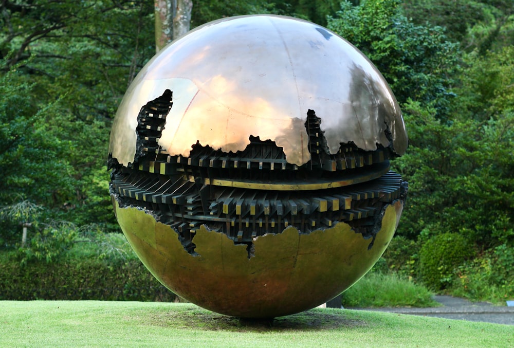 a large metal ball sitting on top of a lush green field