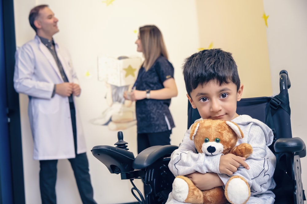 a boy in a wheelchair holding a teddy bear