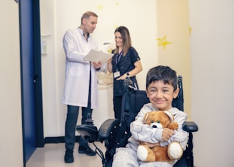a young boy in a wheel chair holding a teddy bear