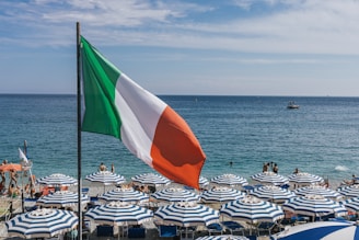 a large italian flag flying over a beach filled with umbrellas