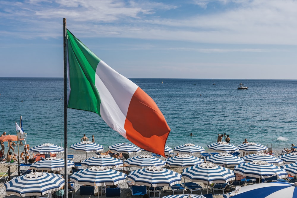 Eine große italienische Flagge weht über einem Strand voller Sonnenschirme
