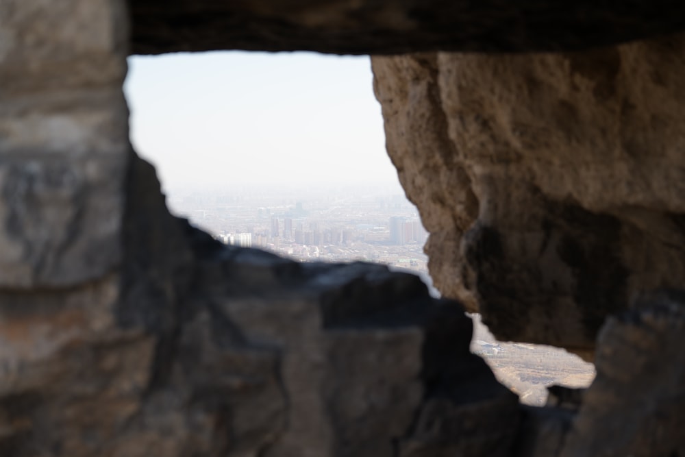 a view of a city through a hole in a rock wall