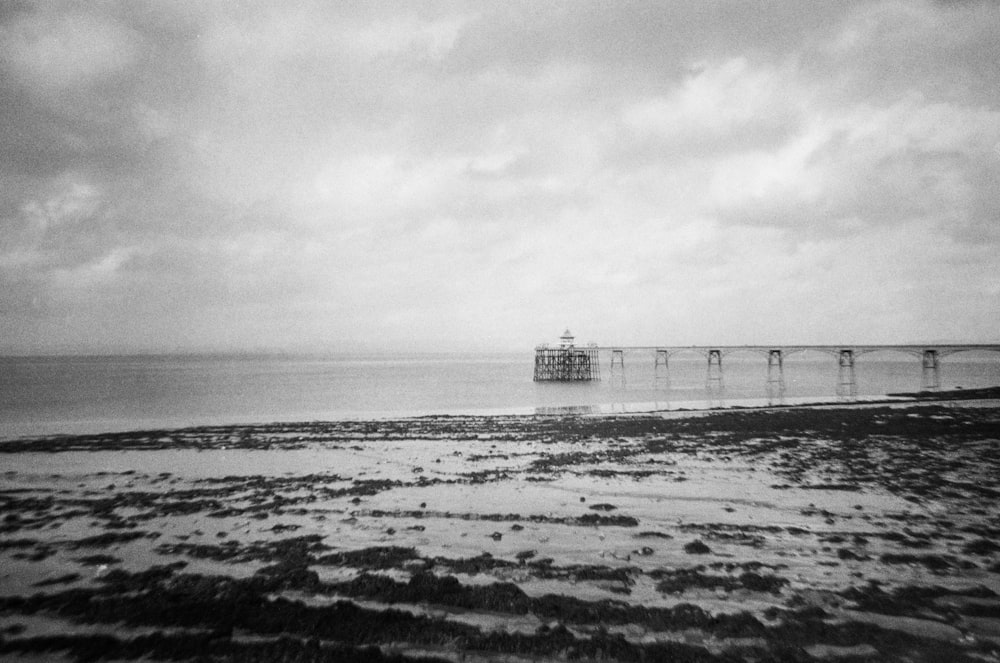 a black and white photo of a beach with a pier in the distance